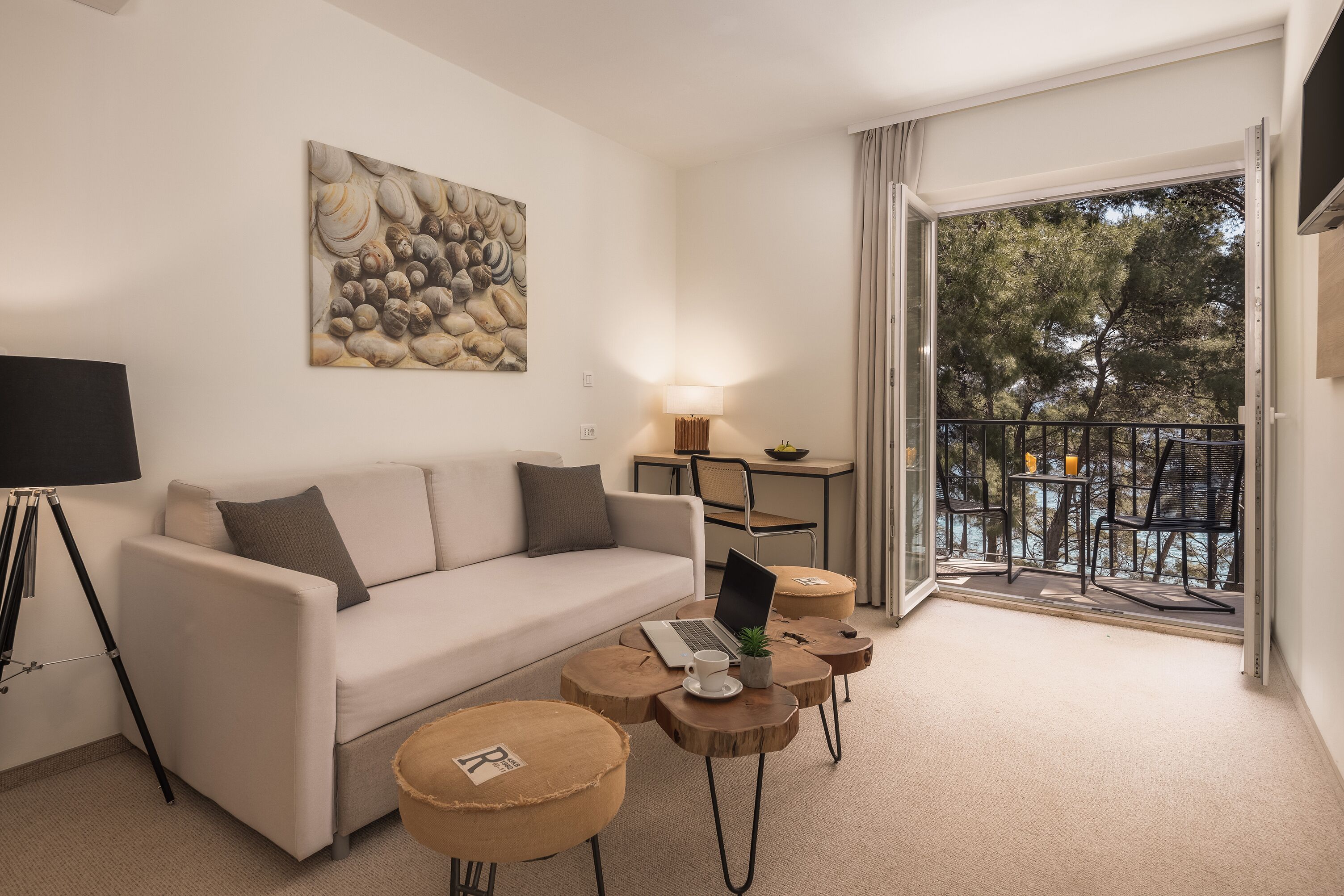 Un salon moderne avec un canapé, un ordinateur portable et une lampe. Il y a un balcon avec des meubles d’extérieur.