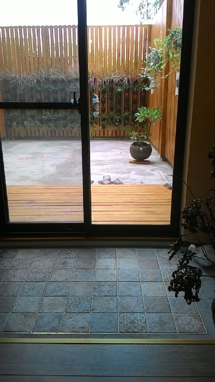 A view through a sliding glass door into a patio area with a wooden fence, potted plants, and a stone-tiled floor.