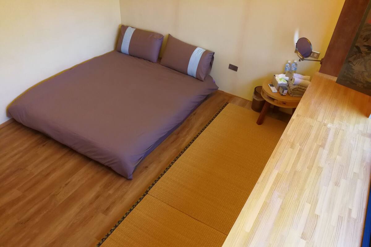 A bedroom with a large bed, a wooden nightstand, and a small table with a mirror and toiletries.