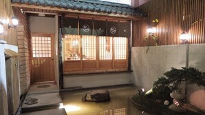 A traditional Japanese entrance with sliding doors, a small garden with a rock, and a lantern. - Sunshiny Castle (Tainan)
