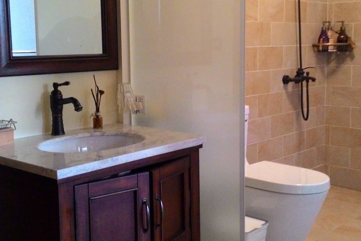 A bathroom with a wooden vanity, a mirror, a sink, a shower, and a toilet.