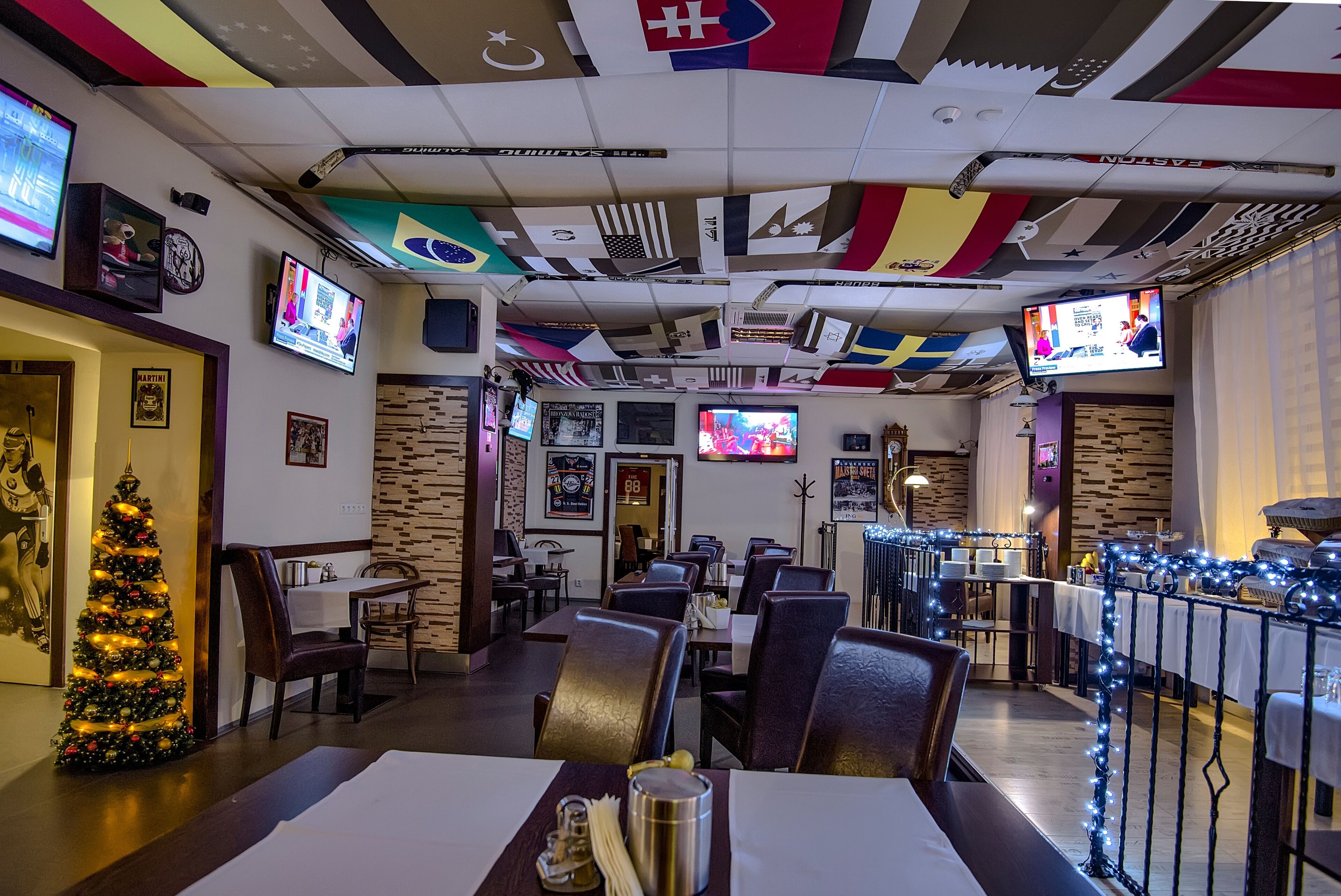 A restaurant with multiple televisions, a Christmas tree, and a variety of flags on the ceiling.