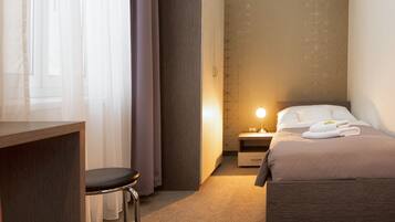 A hotel room with a bed, a desk, a chair, and a nightstand with a lamp.