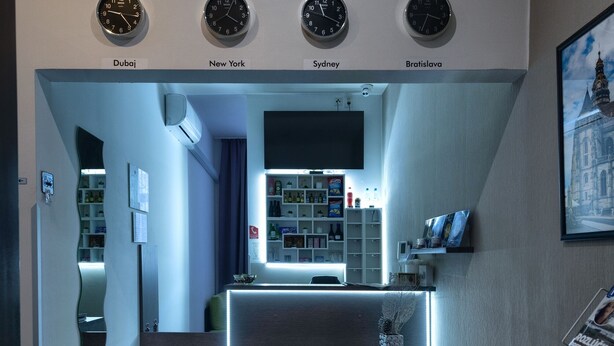 A modern hotel lobby with a reception desk, a sofa, and clocks indicating different cities. - Penzión Sport (Kosice)