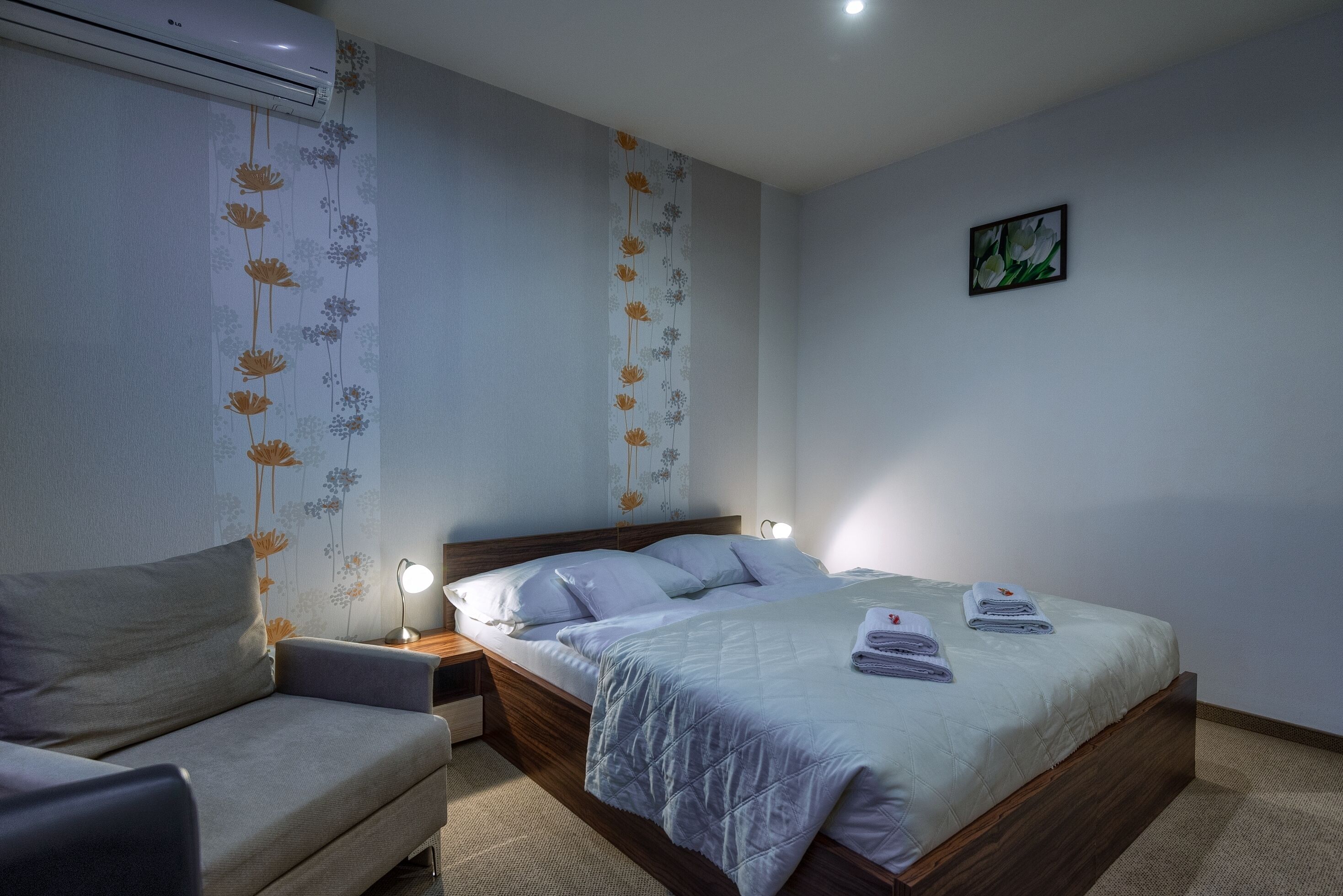 A bedroom with a bed, bedside table, lamp, and a sofa.