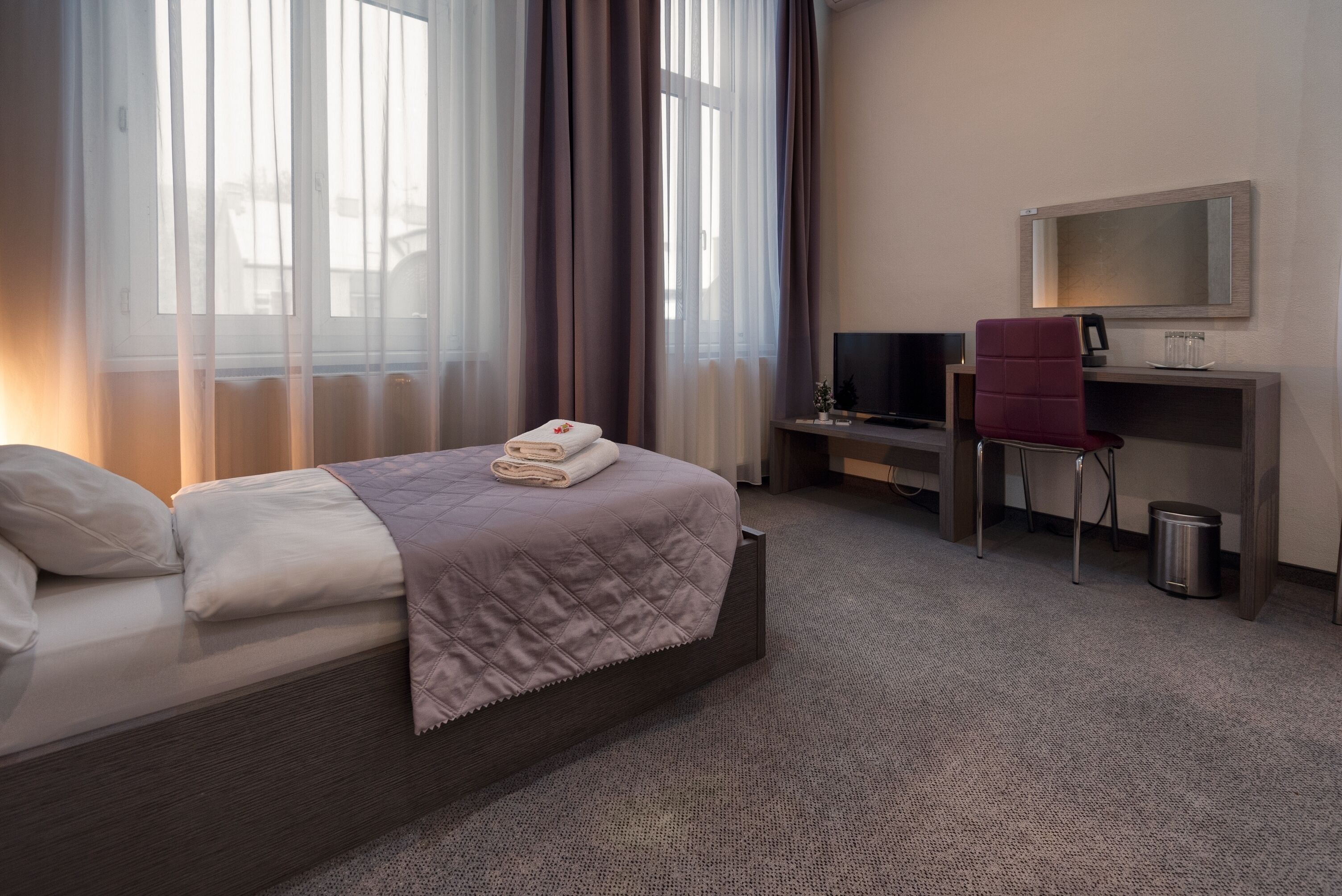 A hotel room with a bed, a desk, a chair, a TV, and a window with curtains.