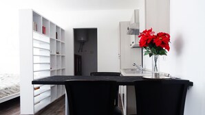 A compact room with a dining table, two chairs, a bookshelf, a kitchen area, and a bed. - Victoria Hotels Royal Garden (Como)