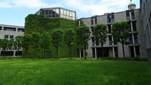 A modern building with a glass structure on top, surrounded by greenery and trees. - Victoria Hotels Royal Garden (Como)