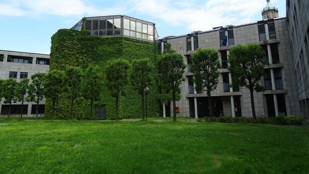 A modern building with a glass structure on top, surrounded by greenery and trees. - Victoria Hotels Royal Garden (Como)