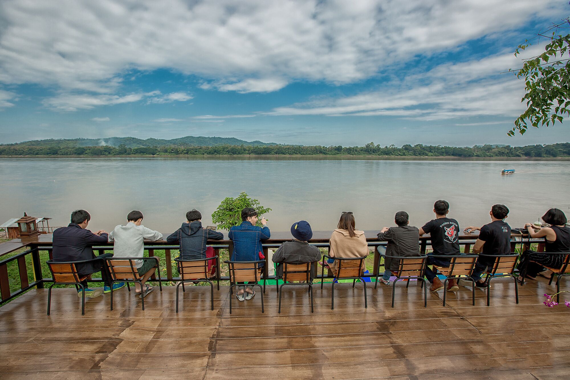 A group of people seated on wooden benches overlooking a calm lake with a distant shoreline.