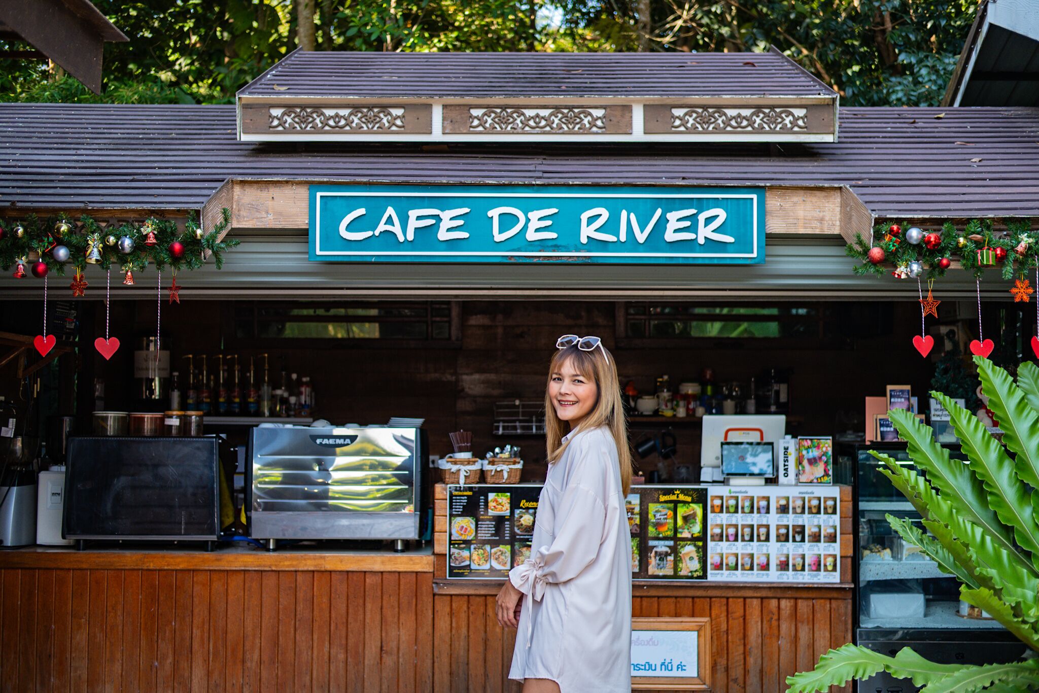 Un café llamado Cafe De River con un mostrador de madera, carteles con el menú y decoración festiva.