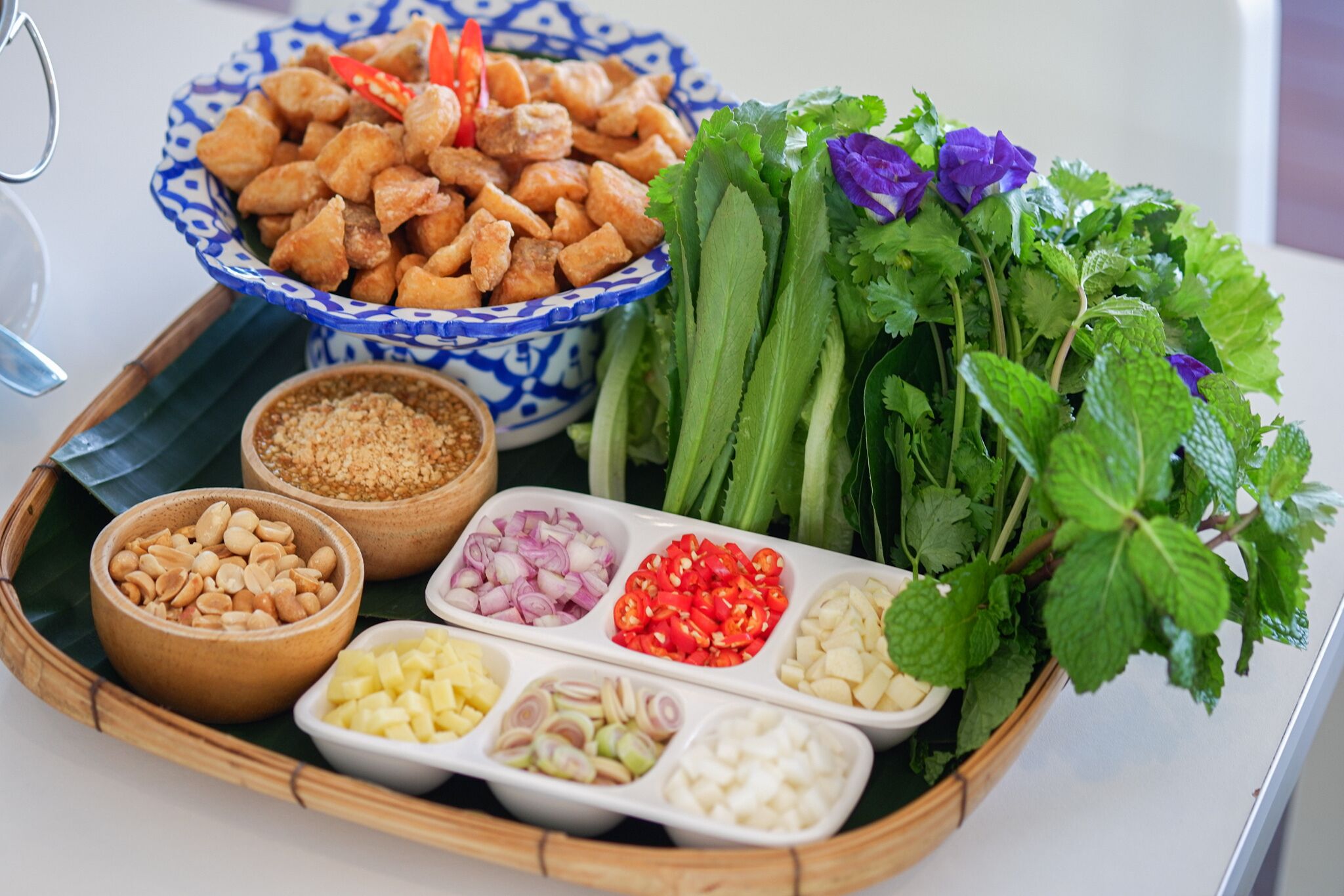 Uma bandeja com diversos alimentos, incluindo frango frito, amendoins, cebola fatiada, pimentas vermelhas e ervas frescas.