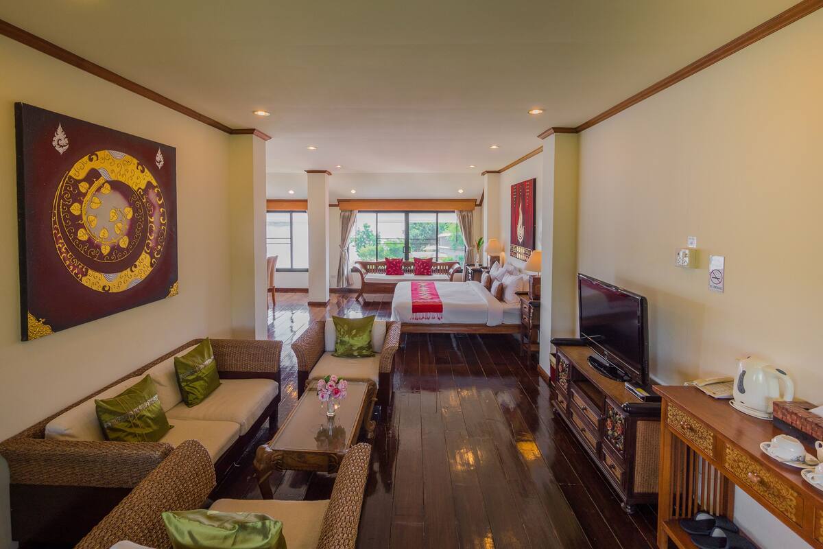 A hotel room with a large bed, a TV, a coffee table with flowers, wicker furniture, and a painting on the wall.