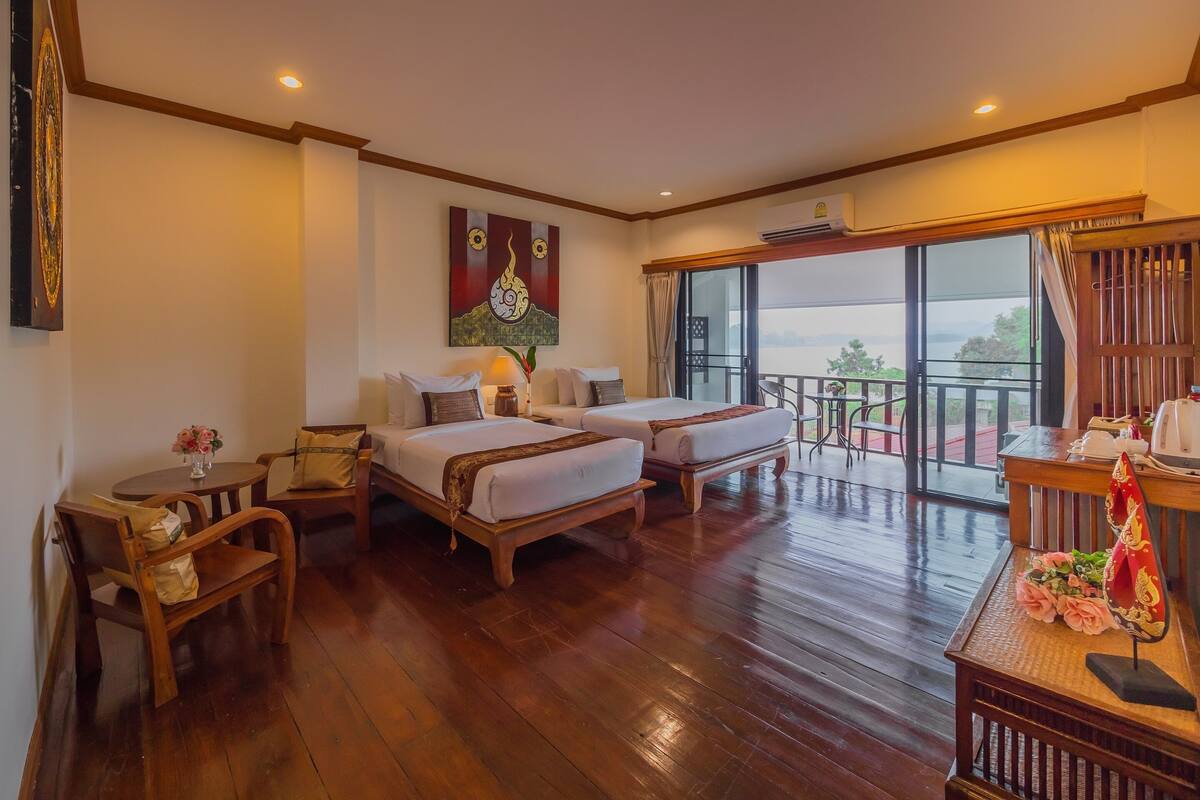 A hotel room with two beds, a balcony with a view, and a wooden floor.