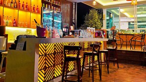Zona de bar con listones de madera en el techo, estantes con botellas y una barra con taburetes.