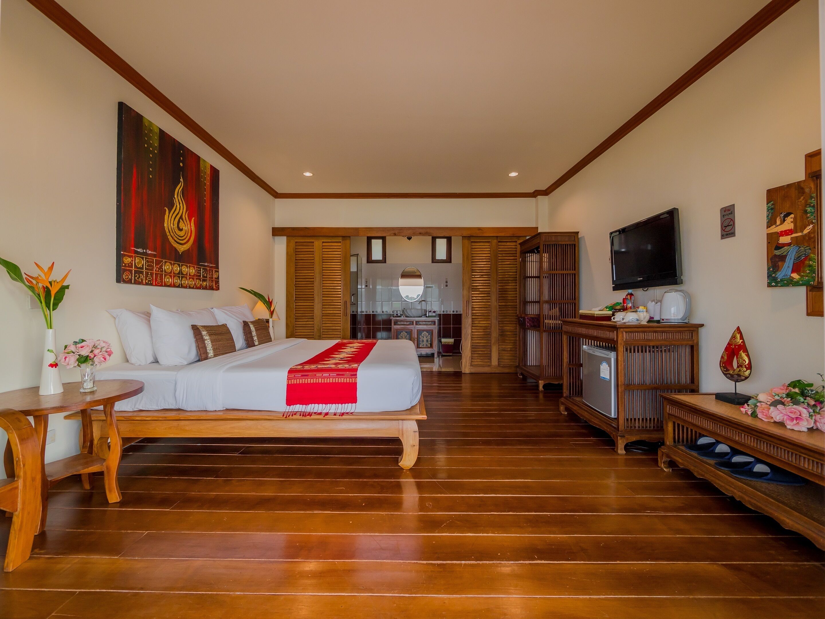 Una camera d'albergo con un letto grande, pavimento in legno, televisione, scrivania e bagno parzialmente visibile attraverso una porta aperta.