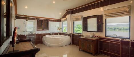 A spacious bathroom with a large bathtub, a double sink vanity, and a large window offering a view of the outdoors.