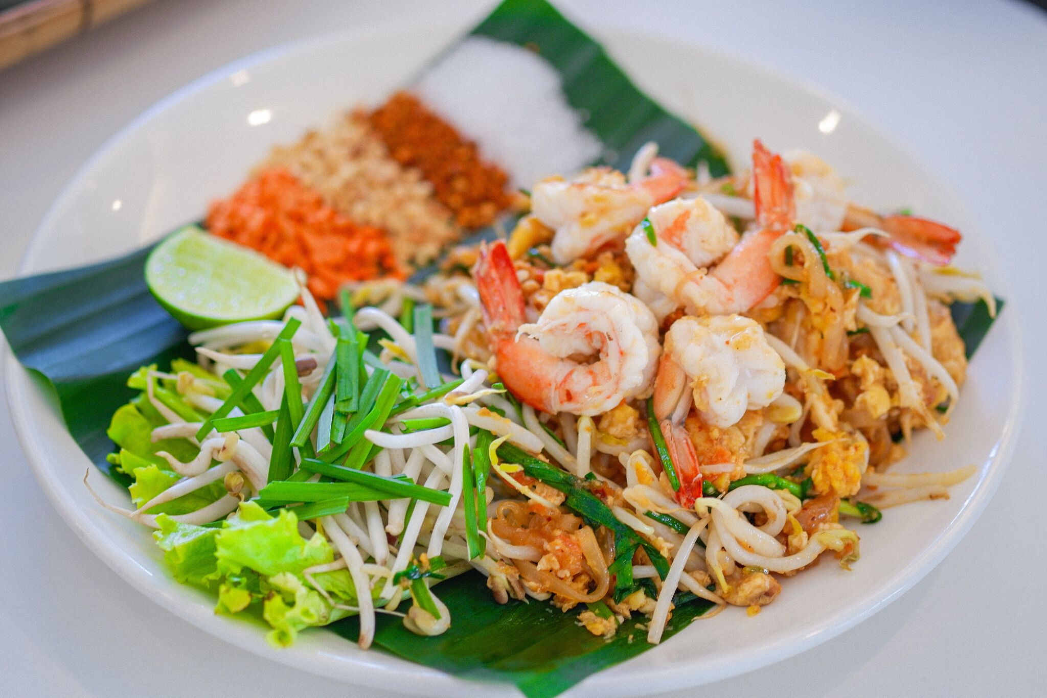Un plato de pad thai con camarones, brotes de soja y lima.