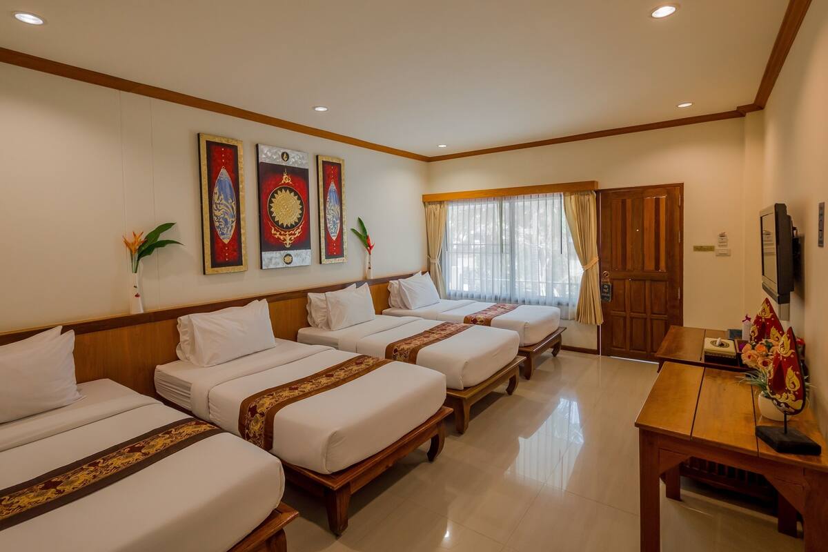 A hotel room with four single beds, a wooden desk, a television, and decorative wall art.