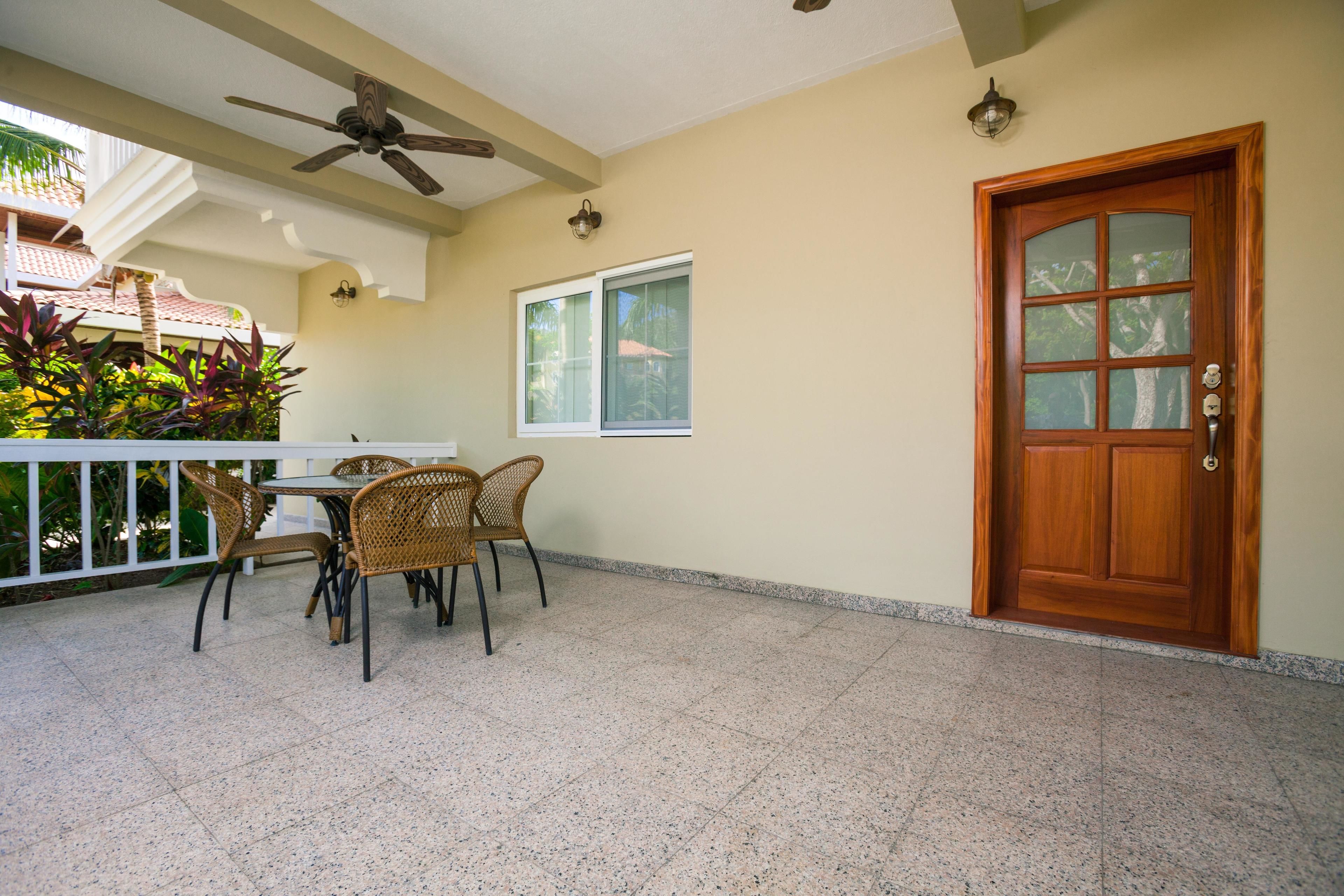A covered patio area with a table and chairs, a ceiling fan, a wooden door, and a window.