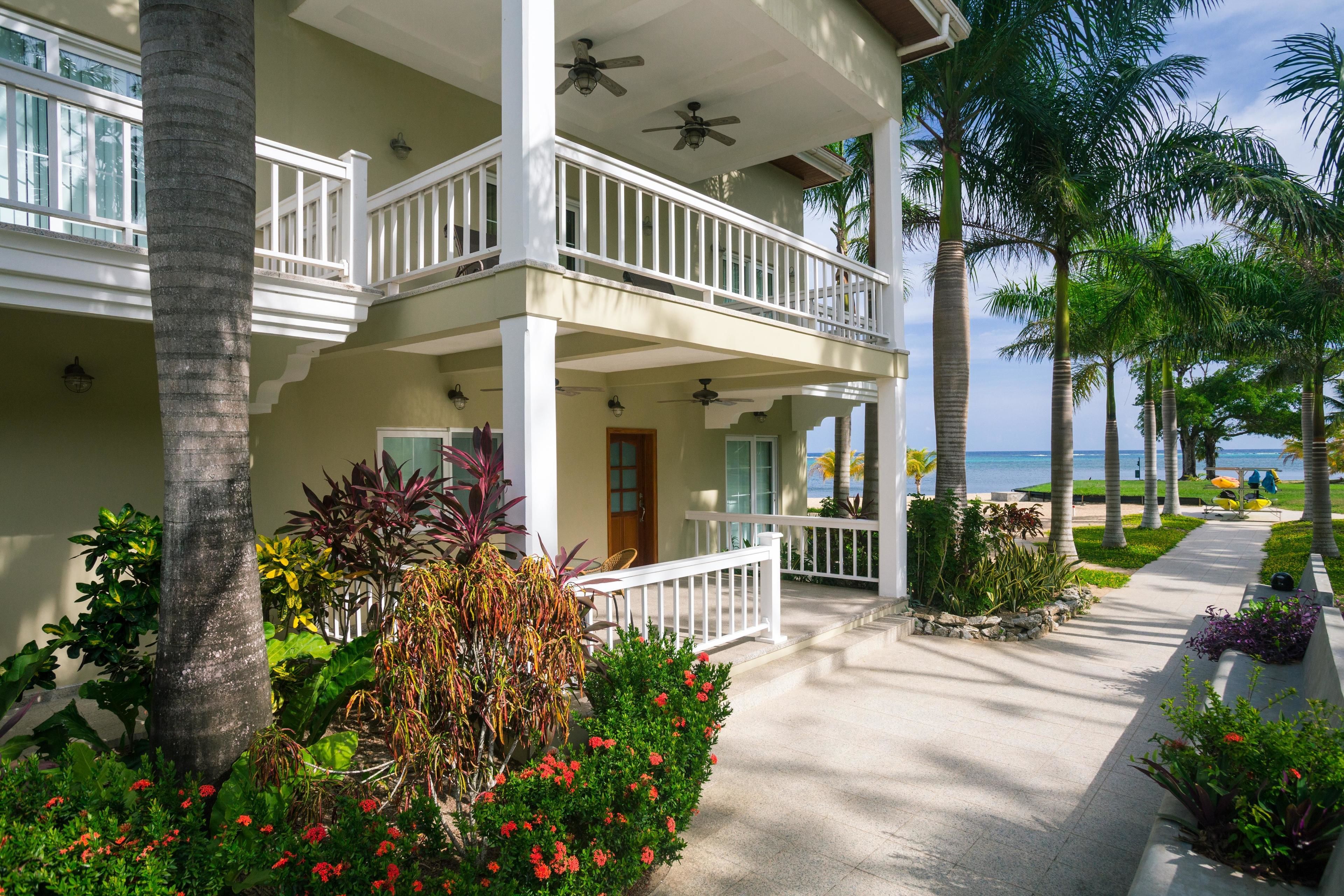 A hotel with a two-story balcony, palm trees, and a pathway leading to the beach.
