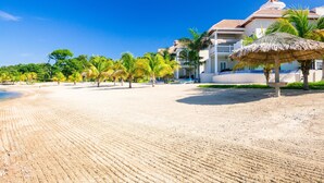 Una playa con un quiosco de paja, palmeras y un edificio con balcones.