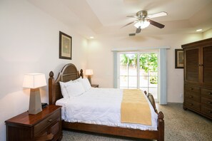 A neatly arranged bedroom with a bed, bedside tables, a ceiling fan, and a view through a window.