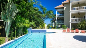 A swimming pool with a tiled edge, surrounded by palm trees and a building with balconies. - Lawson Rock Parrotfish 206 (Roatan)