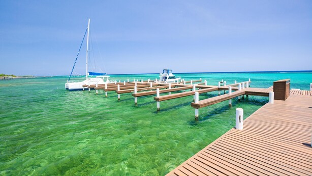 A wooden pier extending into clear turquoise water with a sailboat docked at the end. - Lawson Rock Parrotfish 206 (Roatan)