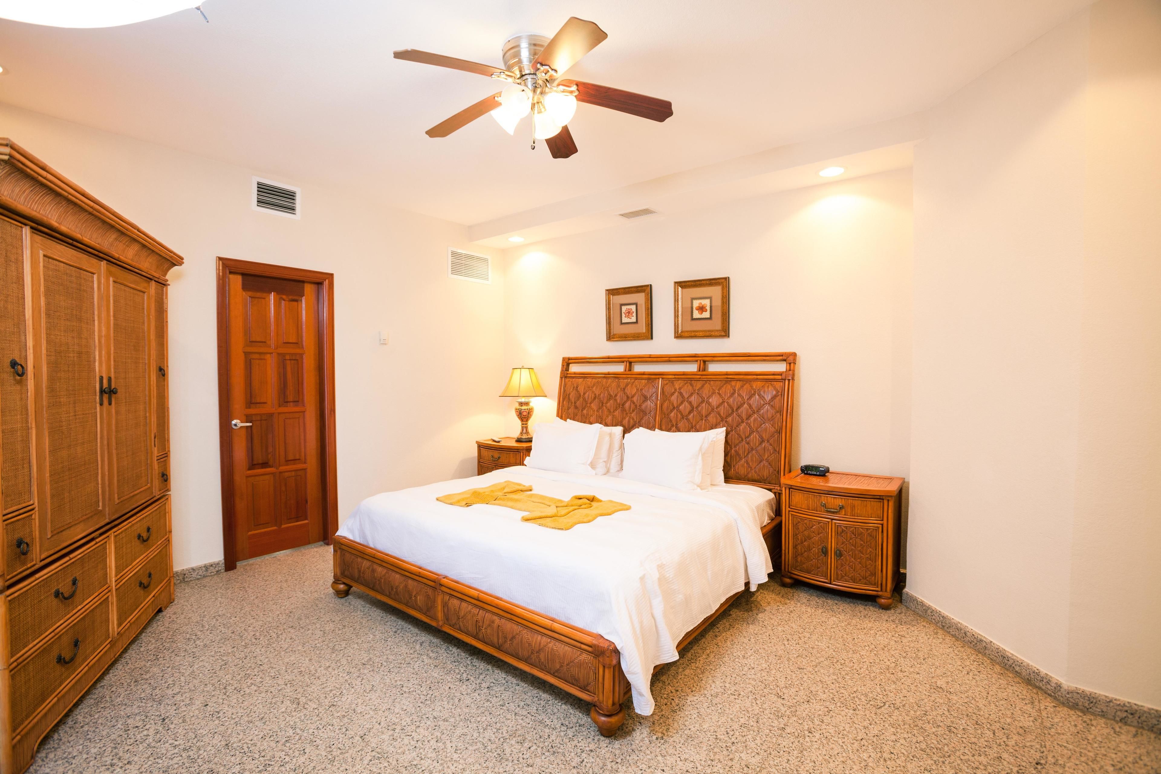 A bedroom with a wooden bed, a ceiling fan, a nightstand, and a wardrobe.