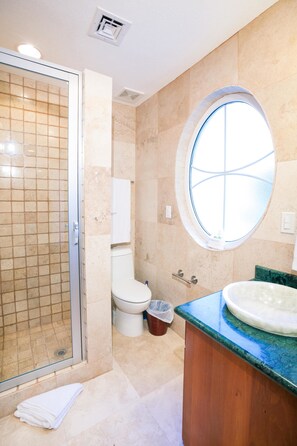 A bathroom with a glass shower enclosure, a round window, a white toilet, and a wooden vanity with a sink.