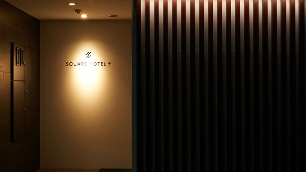 Entrada de un hotel con un cartel que dice "SQUARE HOTEL+".