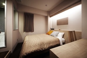 Una camera d'albergo con un letto, una testiera in legno, un comodino e una finestra con tende.