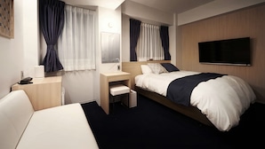 Habitación de hotel con cama, escritorio, silla, televisor y ventana con cortinas.