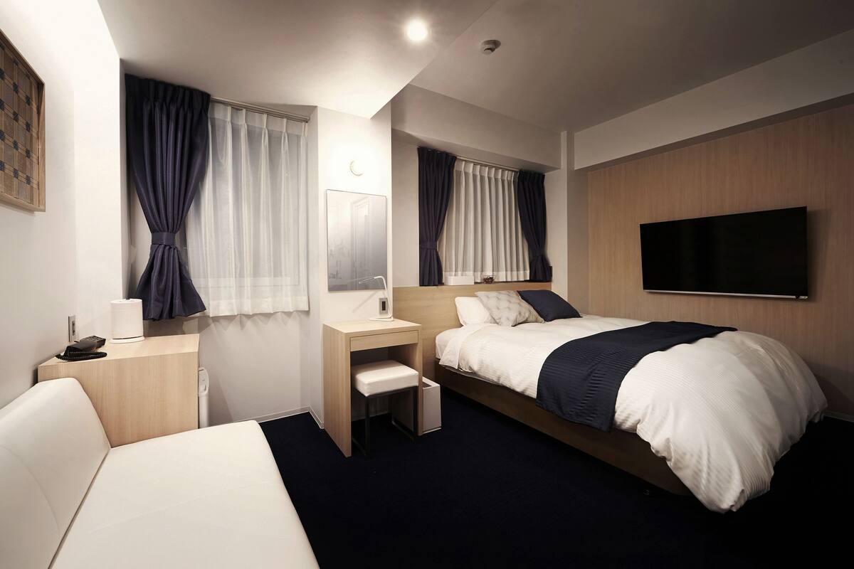 Habitación de hotel con cama, escritorio, silla, televisor y ventana con cortinas.