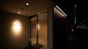 Fachada de un hotel con entrada de vidrio y letreros iluminados.