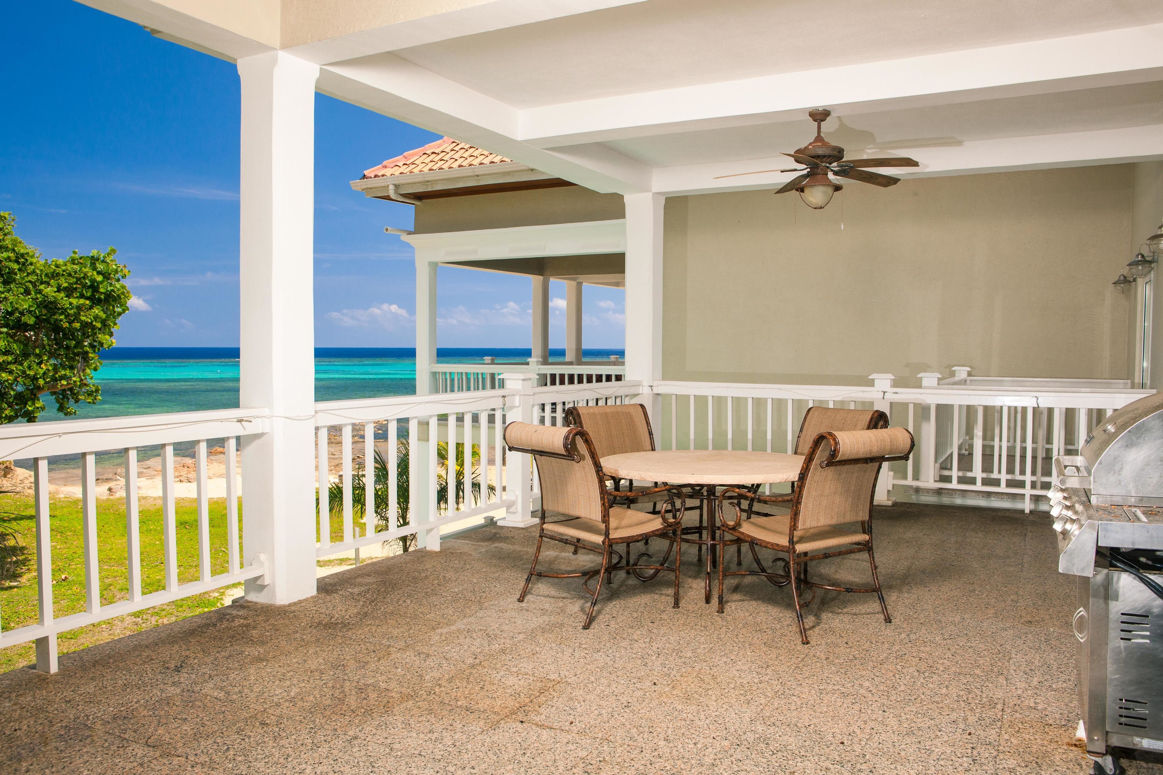 A covered outdoor patio with a table and chairs, a ceiling fan, and a grill.