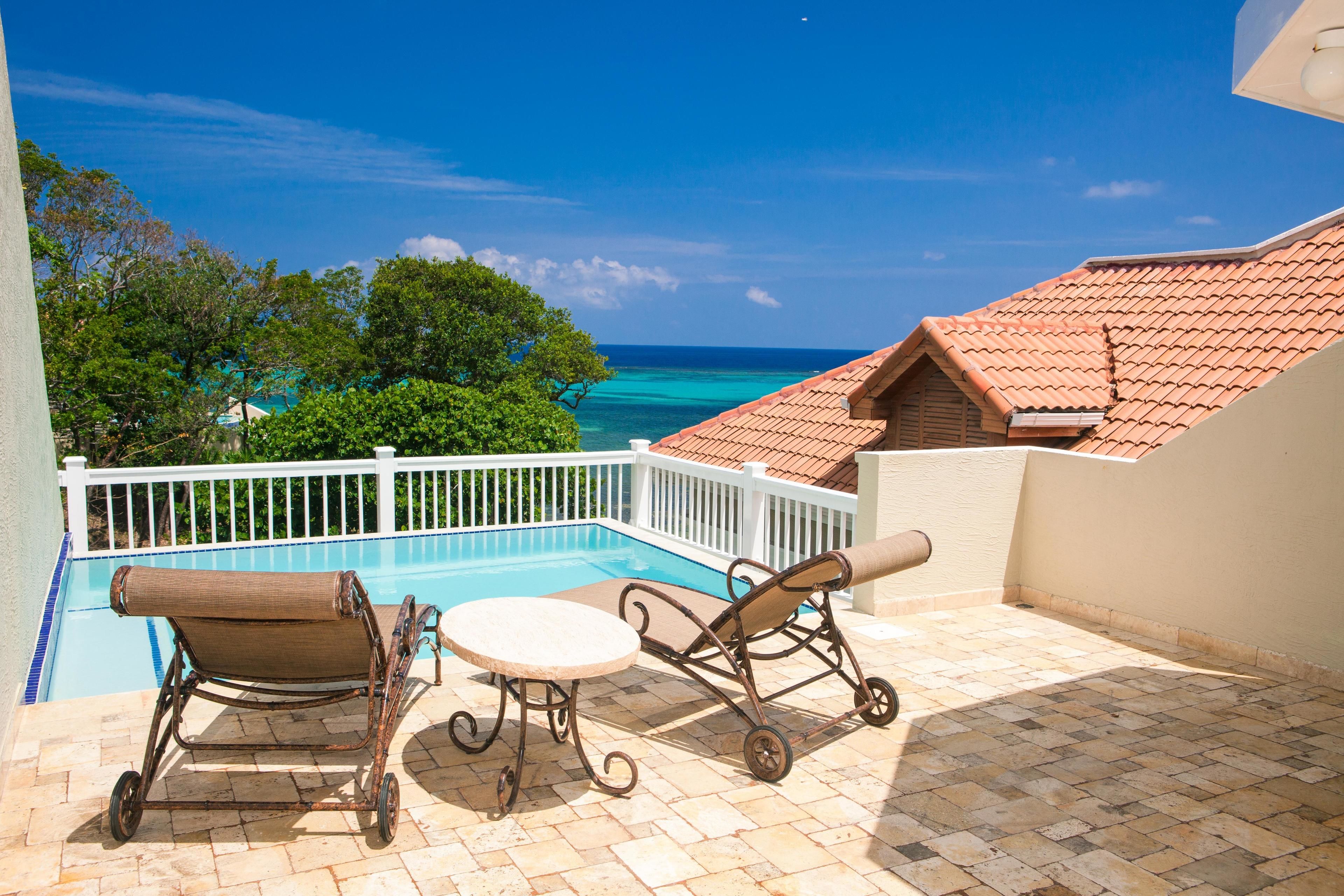 A balcony with a view of a swimming pool and the ocean.