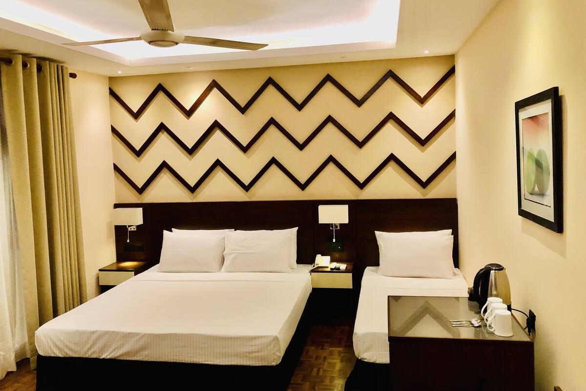 A hotel room with a large bed, two bedside tables, a ceiling fan, and a decorative wall panel.