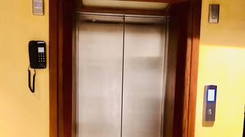 Un ascenseur aux finitions métalliques, encadré de portes en bois et doté d’un sol recouvert de moquette.