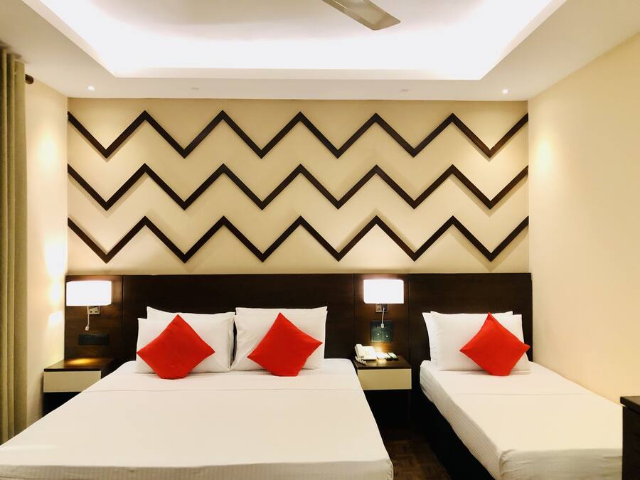 Habitación de hotel con dos camas, cada una con ropa de cama blanca y almohadas rojas, una pared con diseño geométrico moderno tipo chevron y lámparas de noche.
