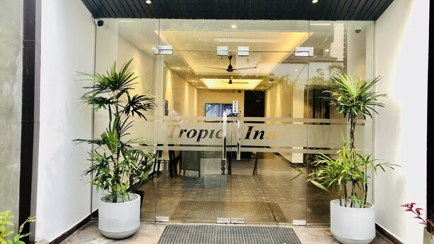 Entrada a Tropic Inn con puertas de vidrio, plantas en macetas, ventilador de techo y piso de baldosas.