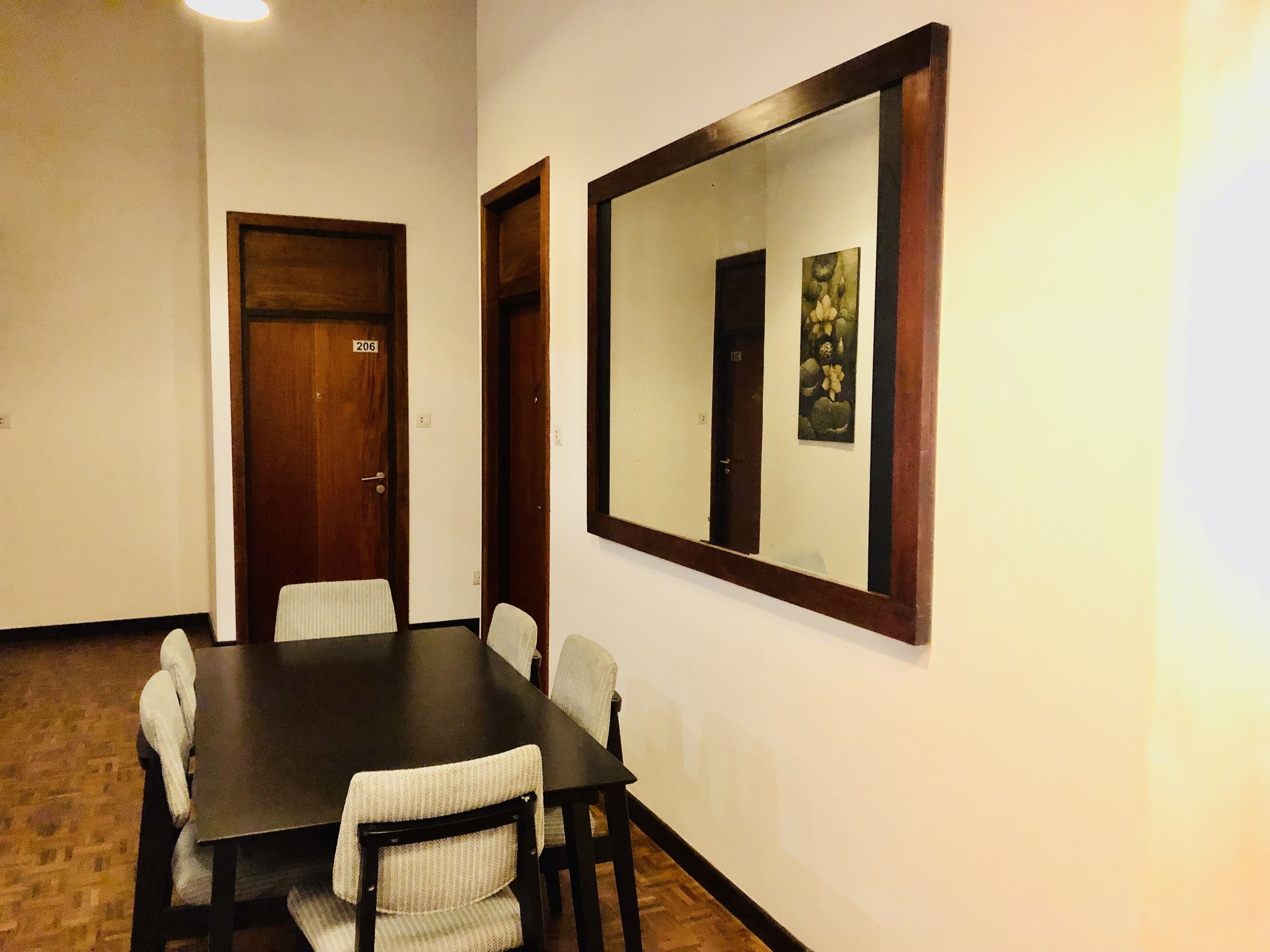 A conference room with a dark wooden table, six chairs, and a large mirror on the wall.