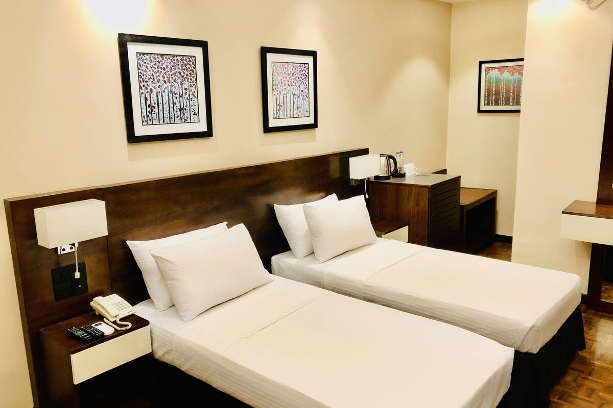 A hotel room with two single beds, a bedside table with a phone, a lamp, and a nightstand with a coffee maker.