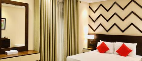 A hotel room with a bed, a nightstand, a mirror, a wooden dresser, and a window with curtains.