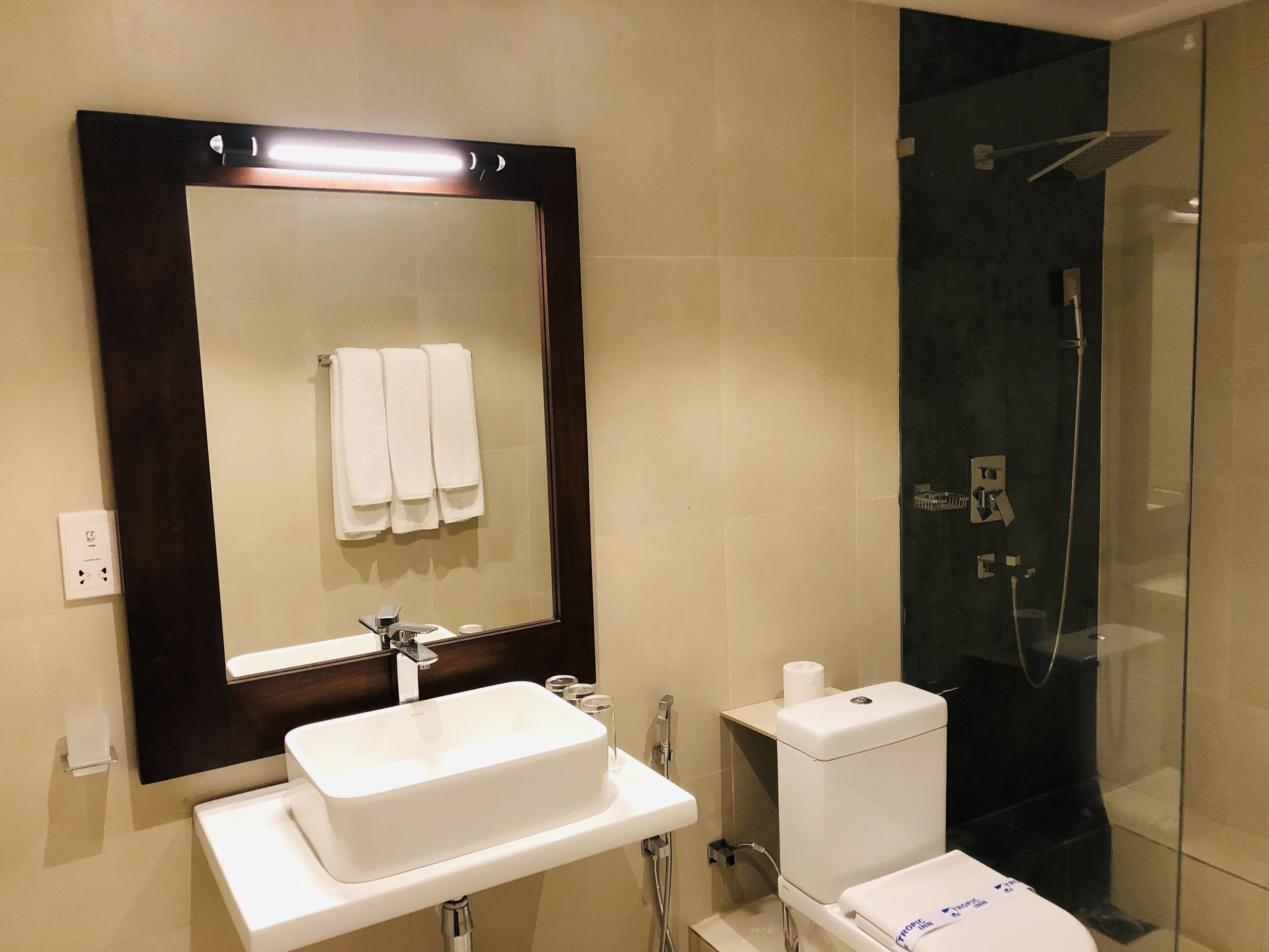 Un baño con lavamanos blanco, espejo y ducha con mampara de vidrio.