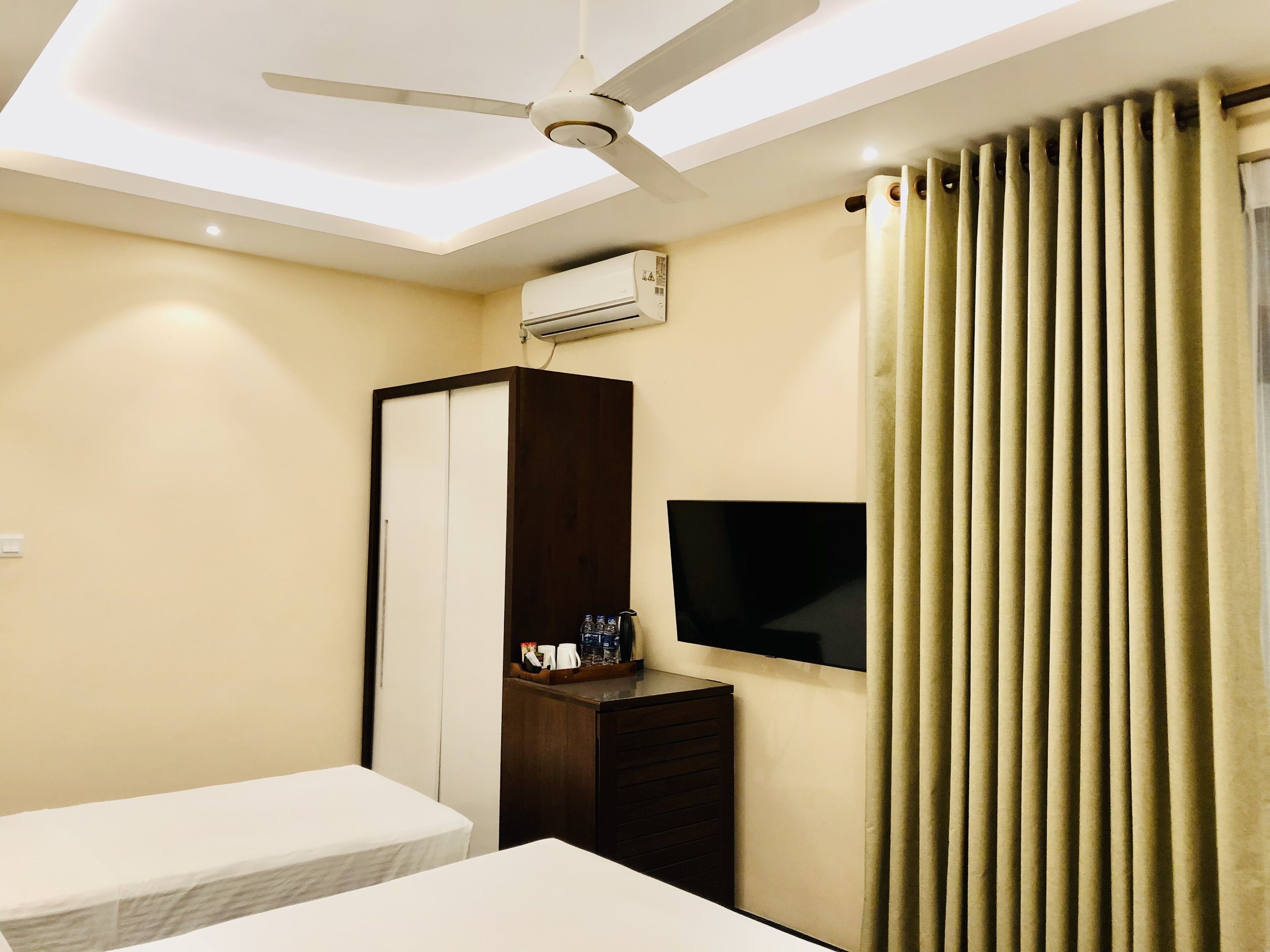 Une chambre d’hôtel équipée d’un lit, d’une armoire, d’une télévision, d’un climatiseur et d’un ventilateur de plafond.