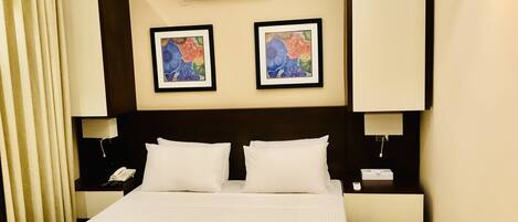 A hotel room with a large bed, two wall-mounted air conditioning units, and two framed floral paintings above the bed.
