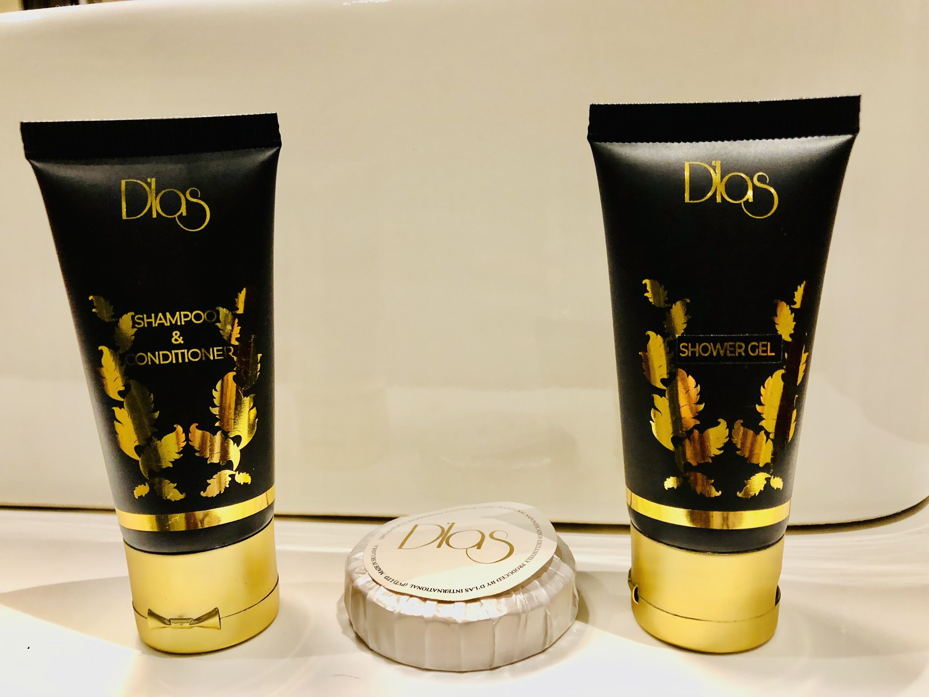 Two black and gold bottles of D'LOS shampoo and conditioner, and shower gel, with a white cap in between.