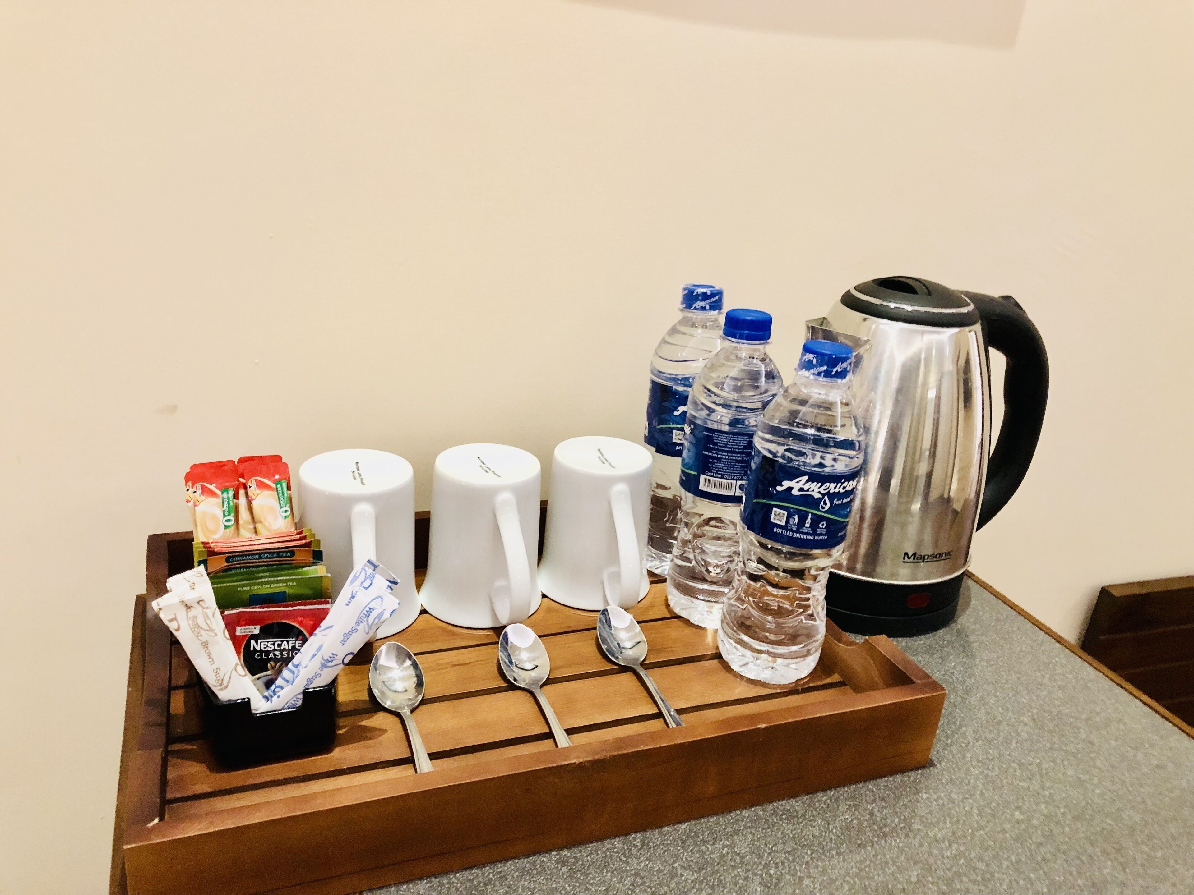 A tray with coffee cups, spoons, a thermos, bottled water, and tea packets.
